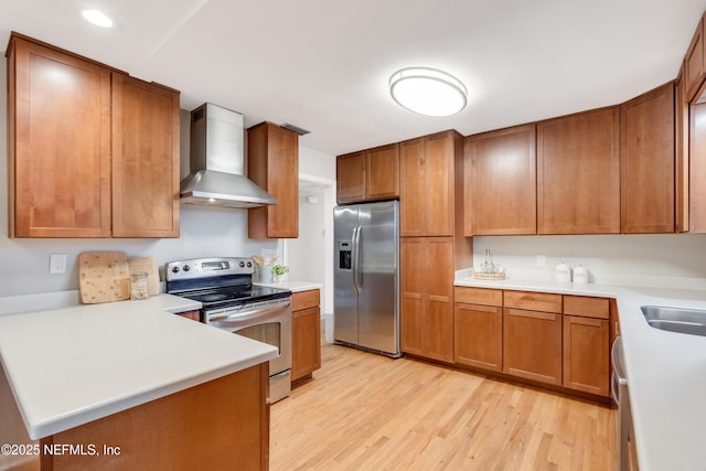 kitchen with appliances with stainless steel finishes, sink, light hardwood / wood-style floors, kitchen peninsula, and wall chimney range hood