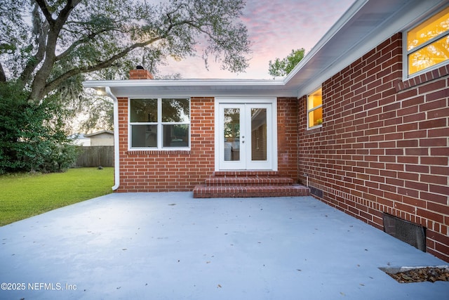 exterior entry at dusk featuring french doors, a patio, and a lawn