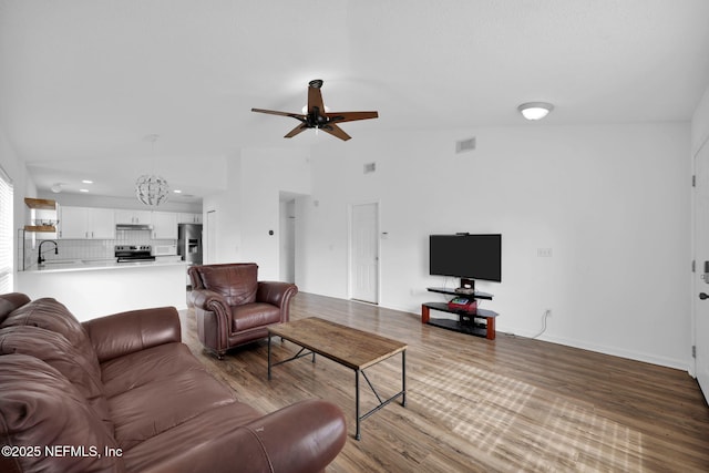 living room with lofted ceiling, sink, ceiling fan with notable chandelier, and light hardwood / wood-style floors