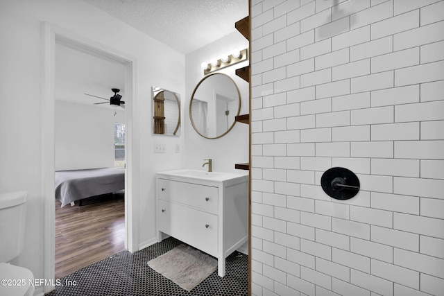 bathroom featuring vanity, tiled shower, ceiling fan, toilet, and a textured ceiling