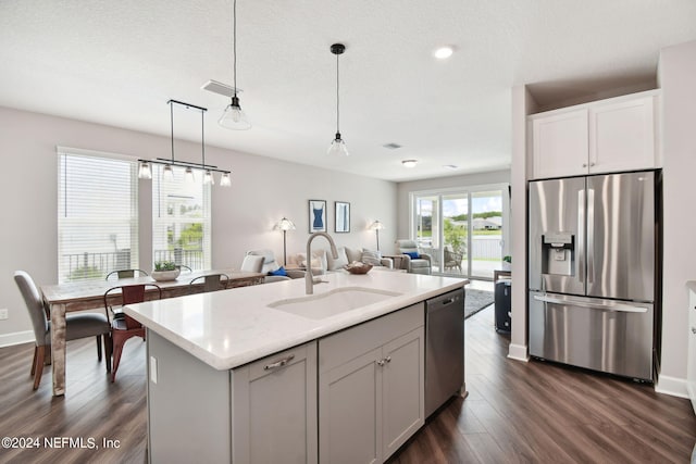 kitchen with a sink, open floor plan, hanging light fixtures, appliances with stainless steel finishes, and dark wood-style floors