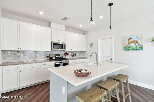 kitchen featuring dark wood-style floors, stainless steel appliances, backsplash, white cabinets, and a kitchen breakfast bar