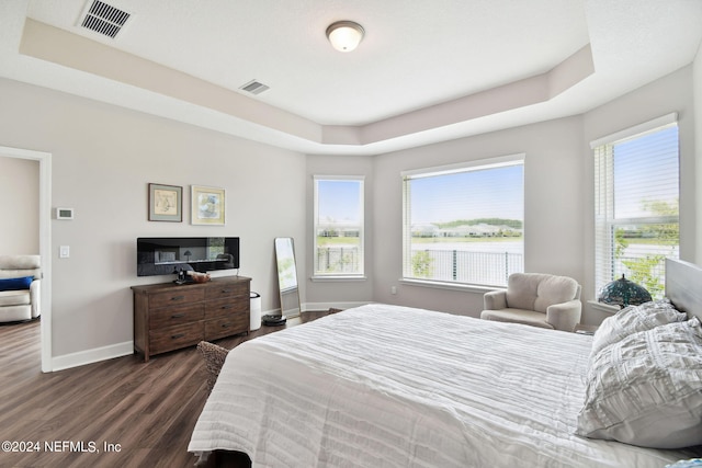 bedroom with a raised ceiling, visible vents, dark wood finished floors, and baseboards