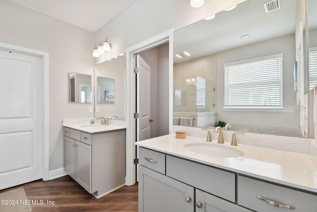 full bath with wood finished floors, tiled shower, a sink, and visible vents