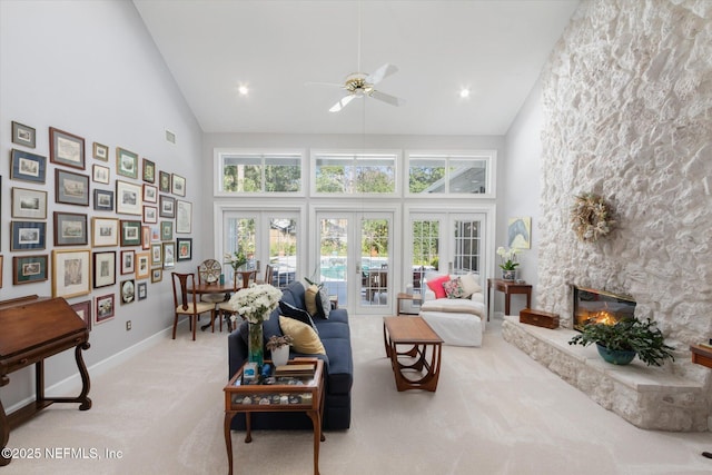 carpeted living room with french doors, ceiling fan, a stone fireplace, and high vaulted ceiling