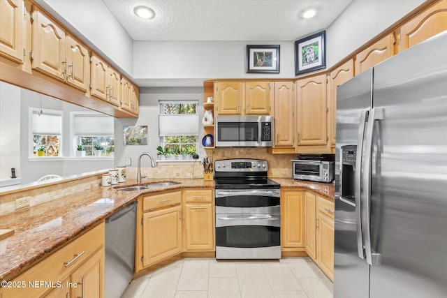 kitchen featuring sink, light tile patterned floors, appliances with stainless steel finishes, light stone counters, and a textured ceiling