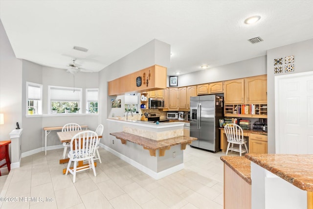 kitchen with built in desk, a breakfast bar area, ceiling fan, kitchen peninsula, and stainless steel appliances