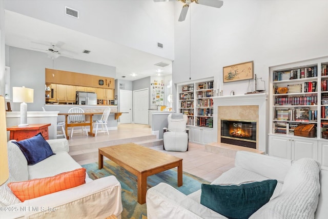 living room featuring a high end fireplace, built in features, ceiling fan, and a high ceiling