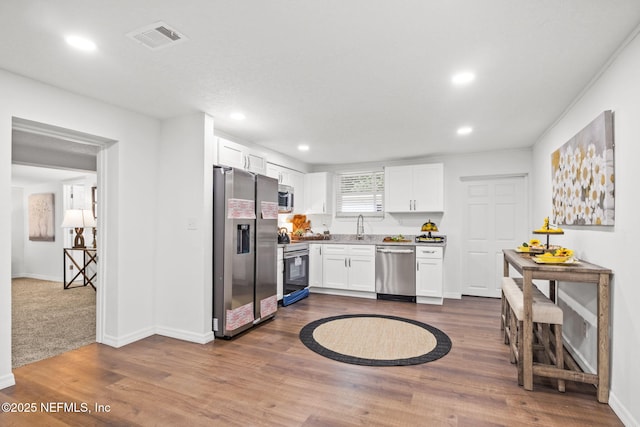 kitchen with dark wood-style flooring, visible vents, appliances with stainless steel finishes, white cabinets, and a sink