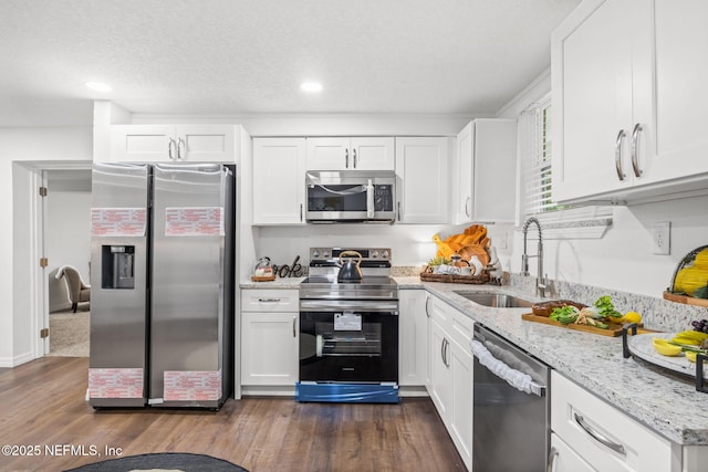 kitchen featuring appliances with stainless steel finishes, a sink, light stone countertops, and white cabinets