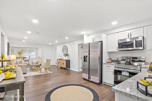 kitchen featuring visible vents, light stone counters, wood finished floors, stainless steel appliances, and white cabinetry