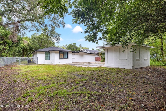 rear view of house featuring a lawn, a patio, concrete block siding, a gate, and fence