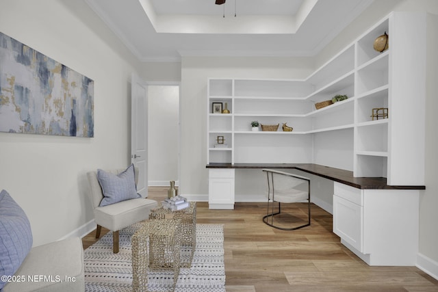 office space with ceiling fan, built in desk, a raised ceiling, and light wood-type flooring