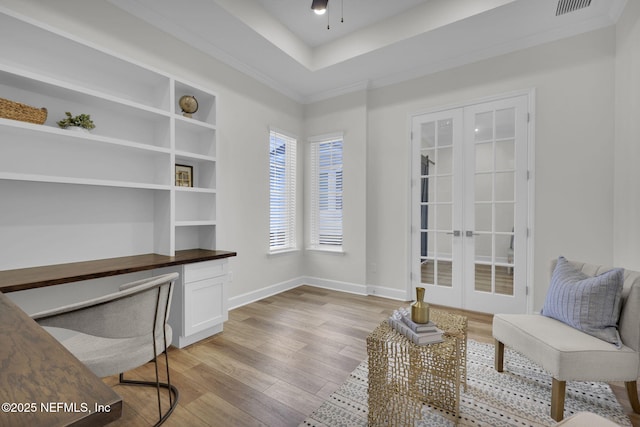 office area featuring built in desk, ornamental molding, light hardwood / wood-style floors, a tray ceiling, and french doors