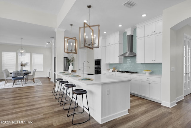 kitchen featuring an inviting chandelier, wall chimney exhaust hood, decorative light fixtures, and white cabinets