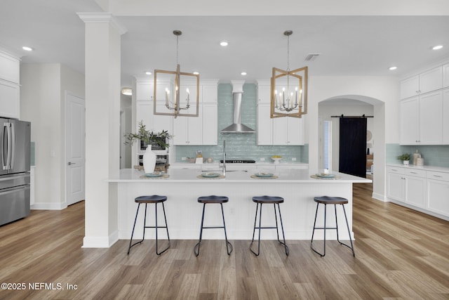 kitchen with stainless steel refrigerator, a barn door, a kitchen breakfast bar, and wall chimney range hood