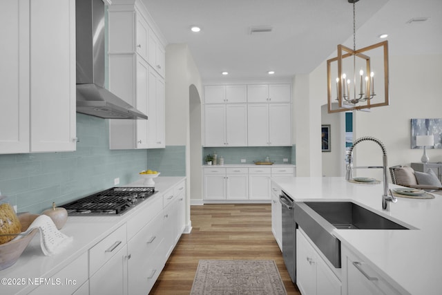 kitchen featuring sink, white cabinetry, decorative light fixtures, stainless steel appliances, and wall chimney range hood