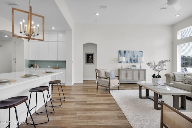 kitchen featuring a breakfast bar, pendant lighting, backsplash, white cabinets, and light wood-type flooring