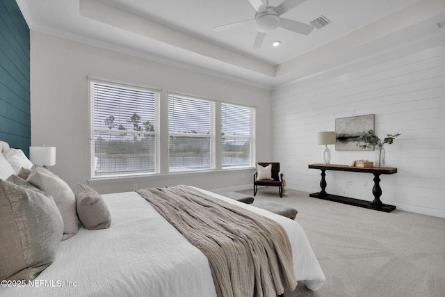 carpeted bedroom with a raised ceiling, ceiling fan, and wood walls