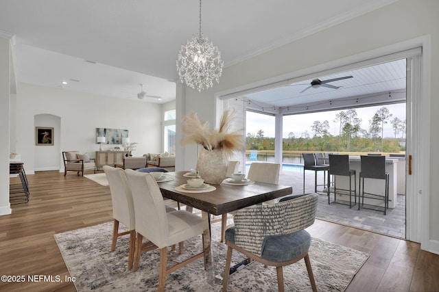 dining space with hardwood / wood-style flooring, ornamental molding, a water view, and ceiling fan with notable chandelier