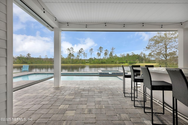 view of swimming pool featuring a patio, a water view, an in ground hot tub, and a bar