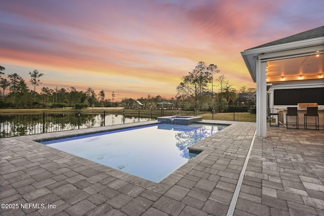 pool at dusk with a water view, an in ground hot tub, exterior bar, and a patio