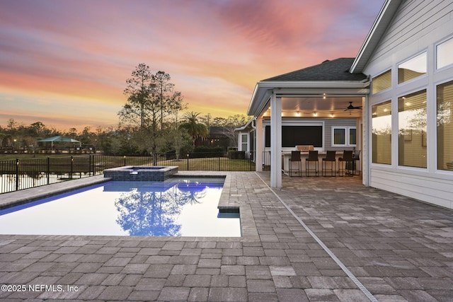 pool at dusk featuring an in ground hot tub, an outdoor bar, and a patio area