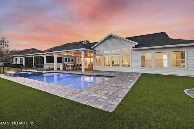 back house at dusk featuring a swimming pool with hot tub, a sunroom, a yard, and a patio area