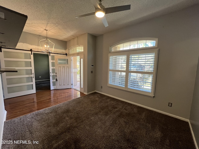 carpeted foyer entrance with a textured ceiling, ceiling fan with notable chandelier, a barn door, and a healthy amount of sunlight