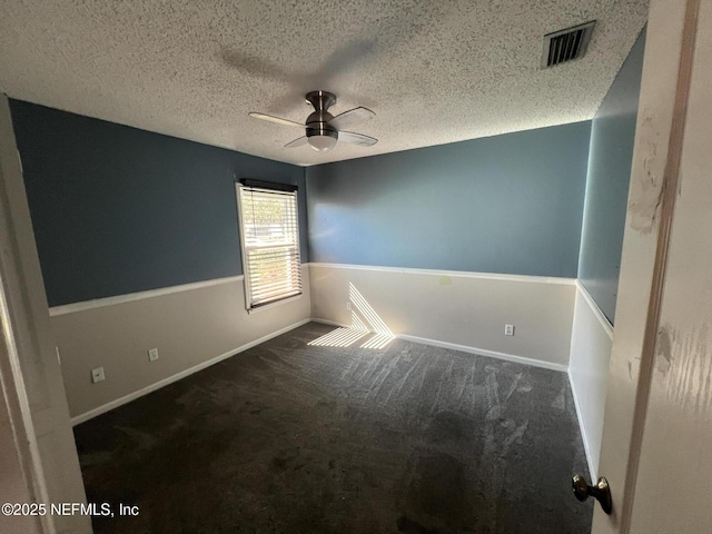 spare room featuring ceiling fan, dark carpet, and a textured ceiling