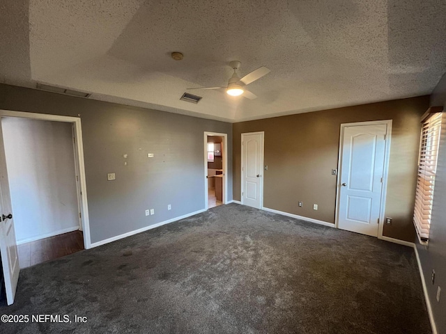 unfurnished bedroom featuring ceiling fan, a tray ceiling, dark carpet, and a textured ceiling