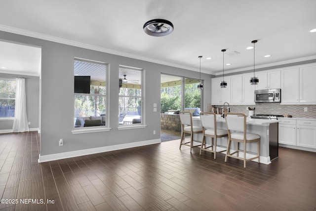 kitchen featuring pendant lighting, dark wood-type flooring, a breakfast bar area, white cabinets, and a center island with sink