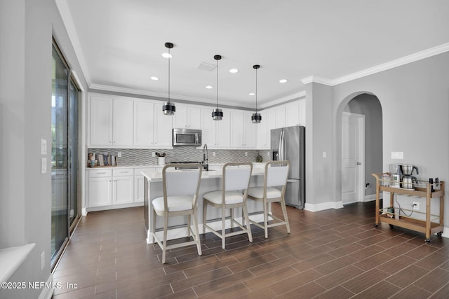 kitchen with crown molding, hanging light fixtures, appliances with stainless steel finishes, decorative backsplash, and white cabinets