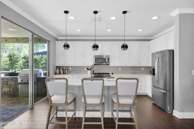 kitchen with white cabinetry, crown molding, hanging light fixtures, a center island with sink, and appliances with stainless steel finishes