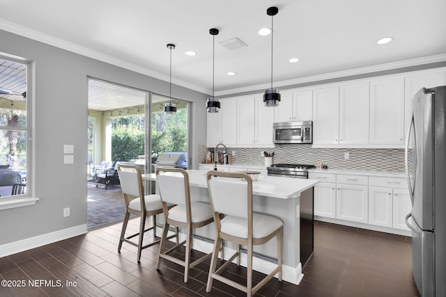 kitchen with white cabinetry, pendant lighting, stainless steel appliances, a kitchen island with sink, and backsplash