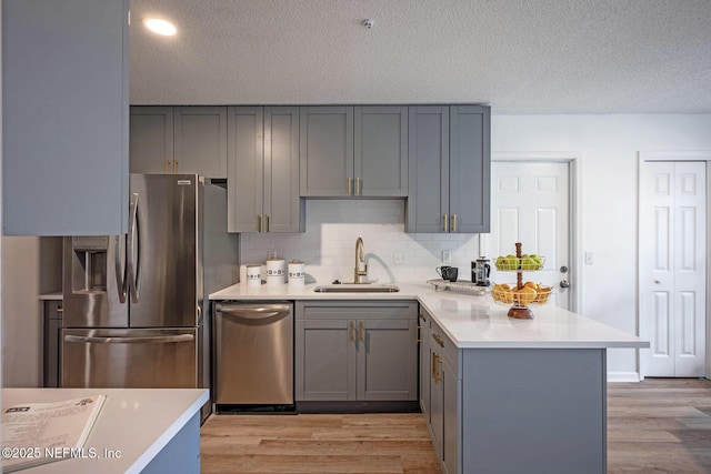 kitchen featuring stainless steel appliances, sink, light hardwood / wood-style floors, and kitchen peninsula