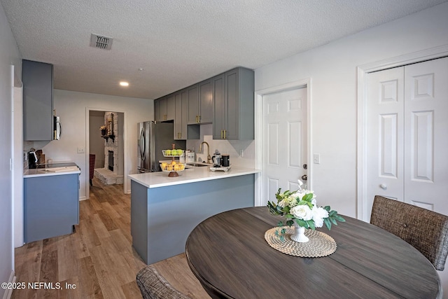 kitchen with sink, light hardwood / wood-style flooring, gray cabinets, kitchen peninsula, and stainless steel appliances