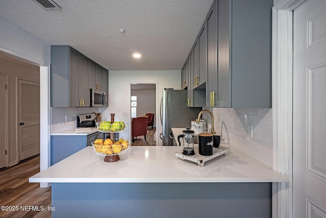 kitchen with stainless steel appliances, a textured ceiling, dark hardwood / wood-style flooring, and kitchen peninsula