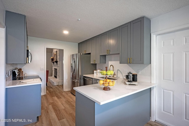 kitchen with gray cabinetry, appliances with stainless steel finishes, kitchen peninsula, and light wood-type flooring