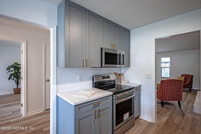 kitchen featuring gray cabinetry, stainless steel appliances, a textured ceiling, decorative backsplash, and light wood-type flooring