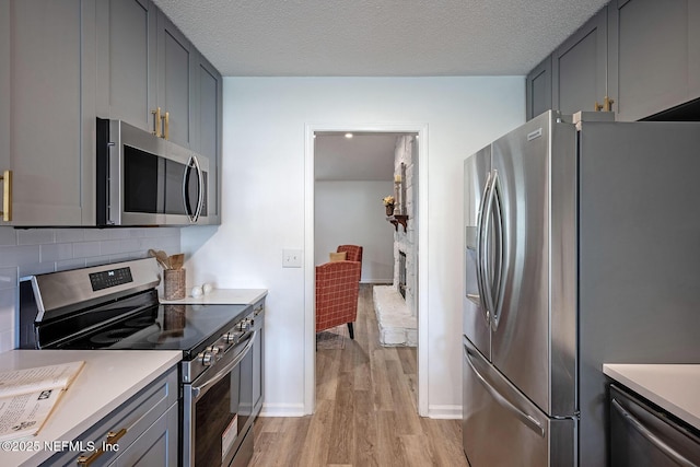 kitchen featuring gray cabinets, stainless steel appliances, tasteful backsplash, a textured ceiling, and light wood-type flooring