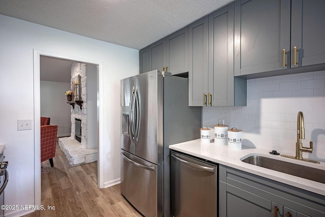 kitchen with stainless steel appliances, a stone fireplace, sink, and gray cabinets