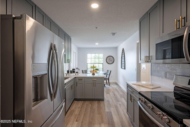 kitchen featuring light hardwood / wood-style flooring, gray cabinets, appliances with stainless steel finishes, backsplash, and kitchen peninsula