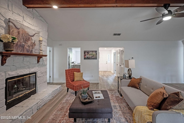 living room featuring a fireplace, light hardwood / wood-style floors, and vaulted ceiling with beams