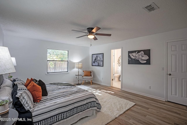 bedroom featuring ceiling fan, hardwood / wood-style flooring, ensuite bath, and a textured ceiling