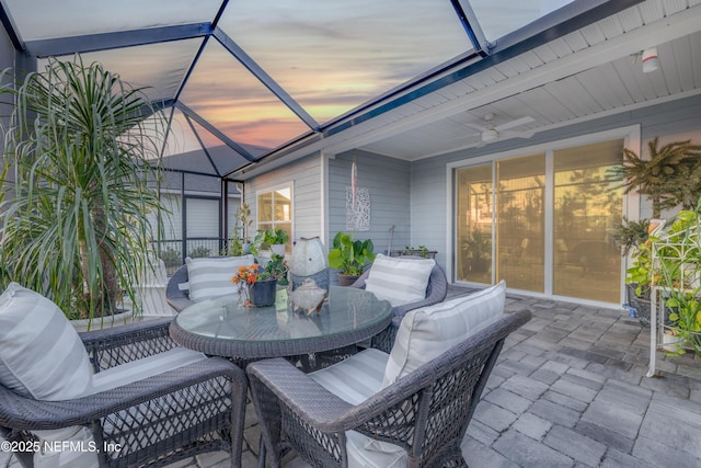 patio terrace at dusk featuring ceiling fan and glass enclosure