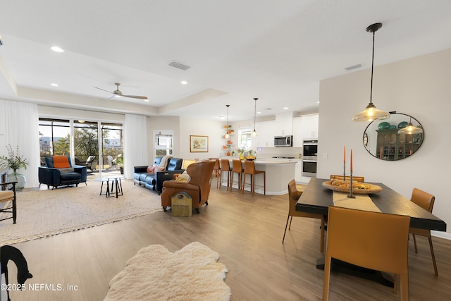 living room featuring ceiling fan, light hardwood / wood-style floors, and a tray ceiling