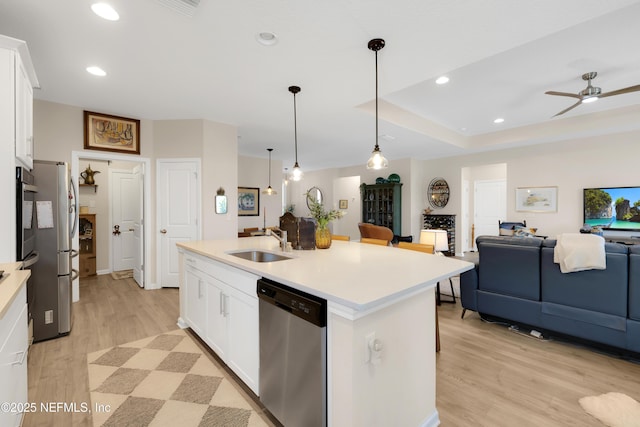 kitchen with sink, a kitchen island with sink, hanging light fixtures, stainless steel appliances, and white cabinets