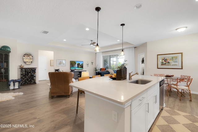 kitchen featuring decorative light fixtures, white cabinetry, sink, a kitchen island with sink, and a raised ceiling