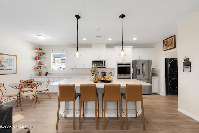 kitchen with stainless steel appliances, stacked washer and clothes dryer, a center island, and pendant lighting